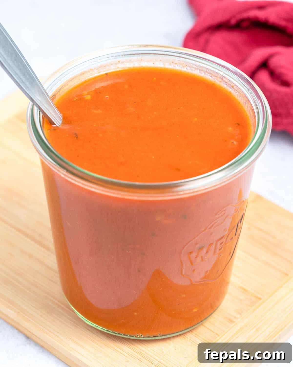 a jar with red enchilada sauce with a spoon in the jar.