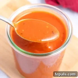 a jar filled with red enchilada sauce with a spoonful over the jar.