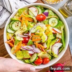 a hand holding a bowl with garden salad mixed with dressing.