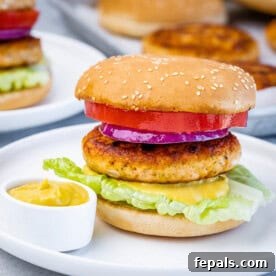 A salmon burger on a white plate with a small bowl of mustard.