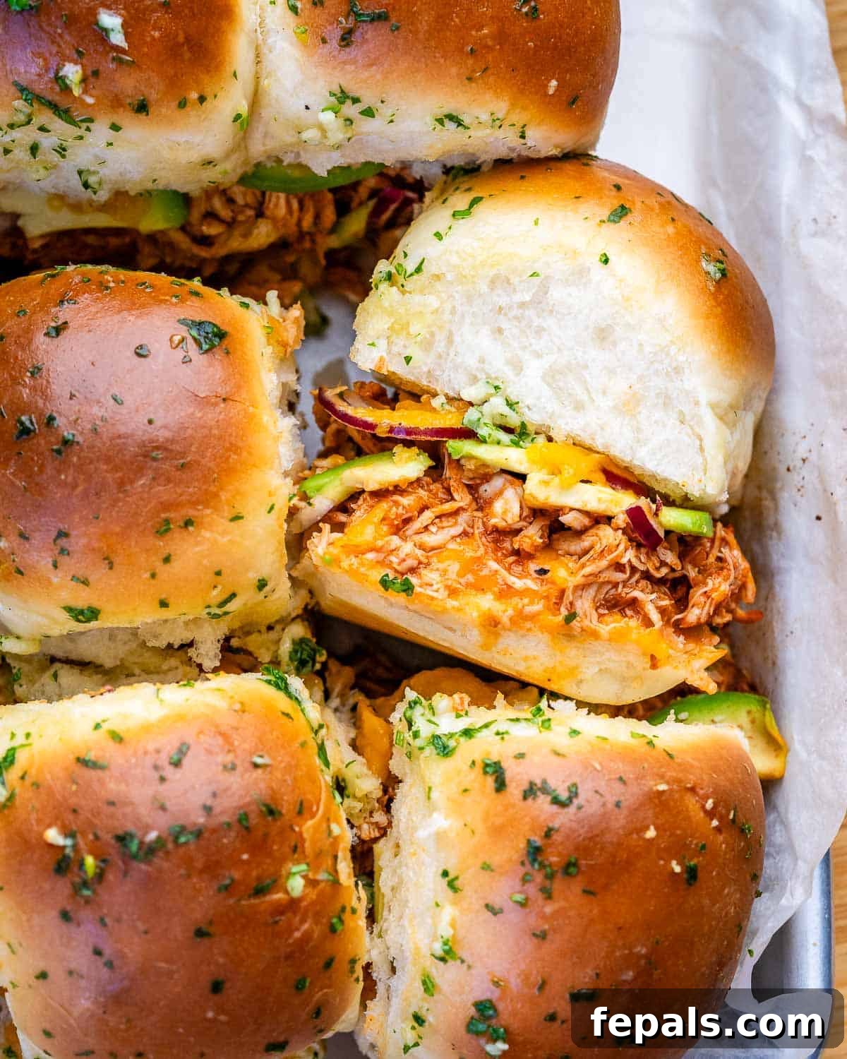 BBQ chicken sliders with avocado in a parchment-lined tray.