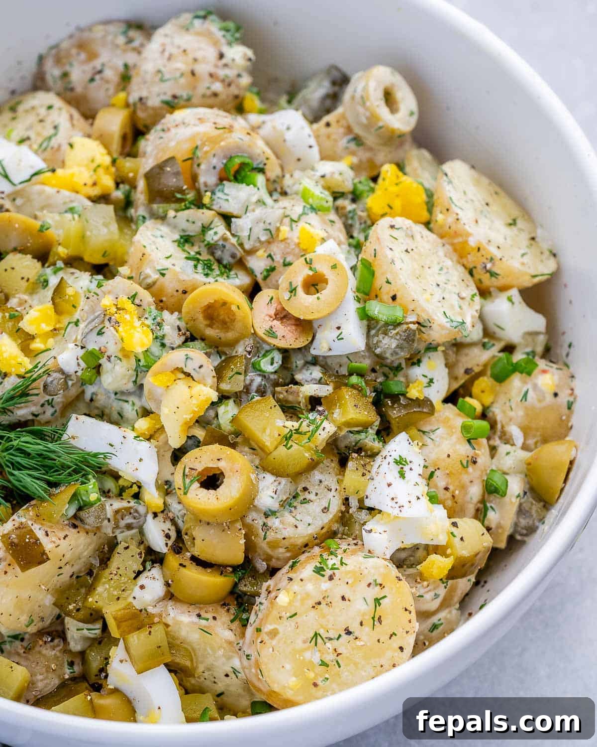 A white bowl with dill pickle potato salad.