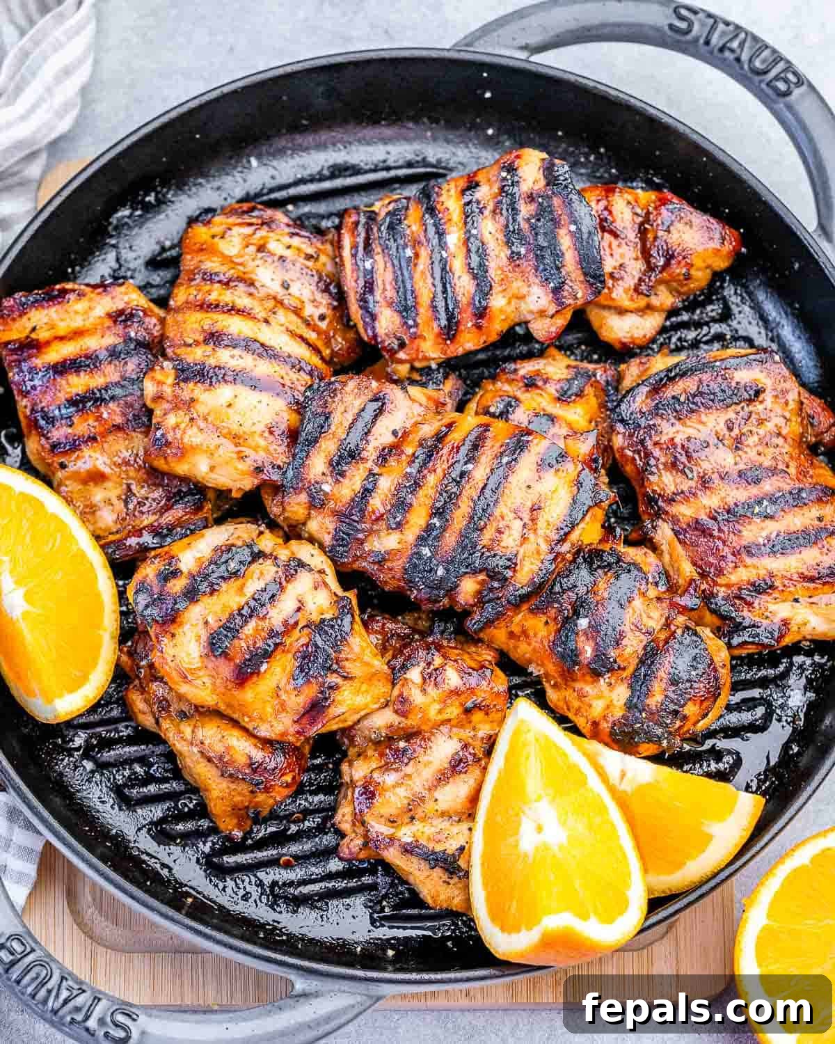 a grill pan with grilled chicken thighs and orange slices as garnishes.