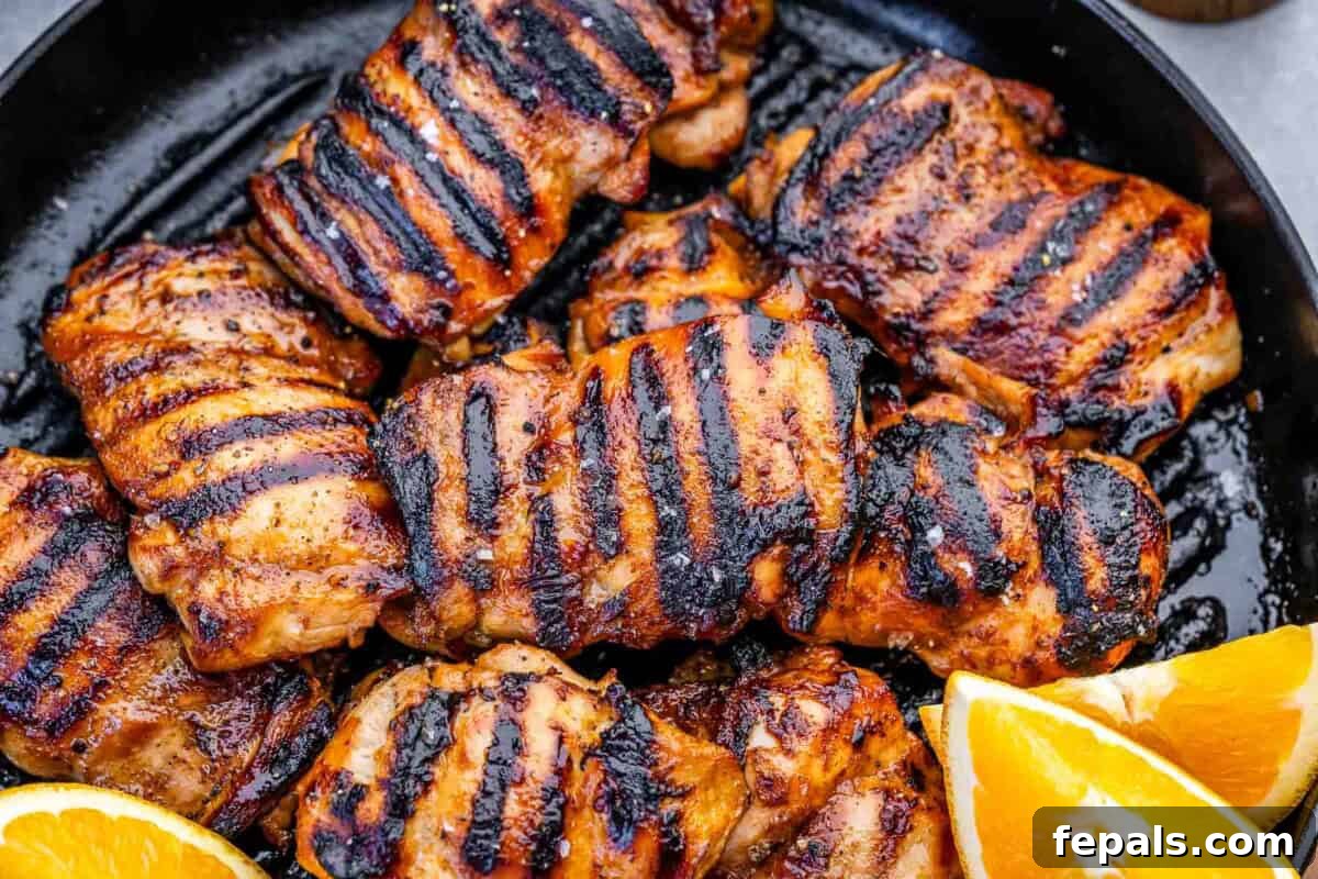 grilled chicken thighs on a pan with slices of oranges next to them.
