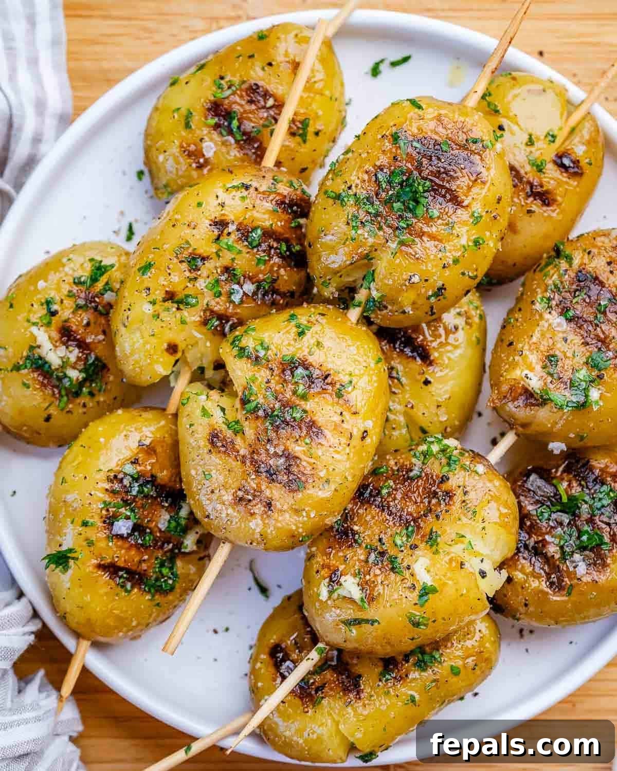 A white plate of grilled potatoes brushed with garlic parsley sauce.