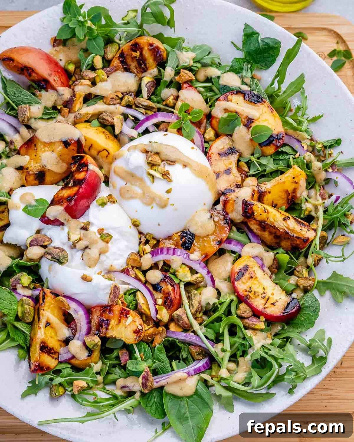 A peach burrata salad with arugula on a white plate.