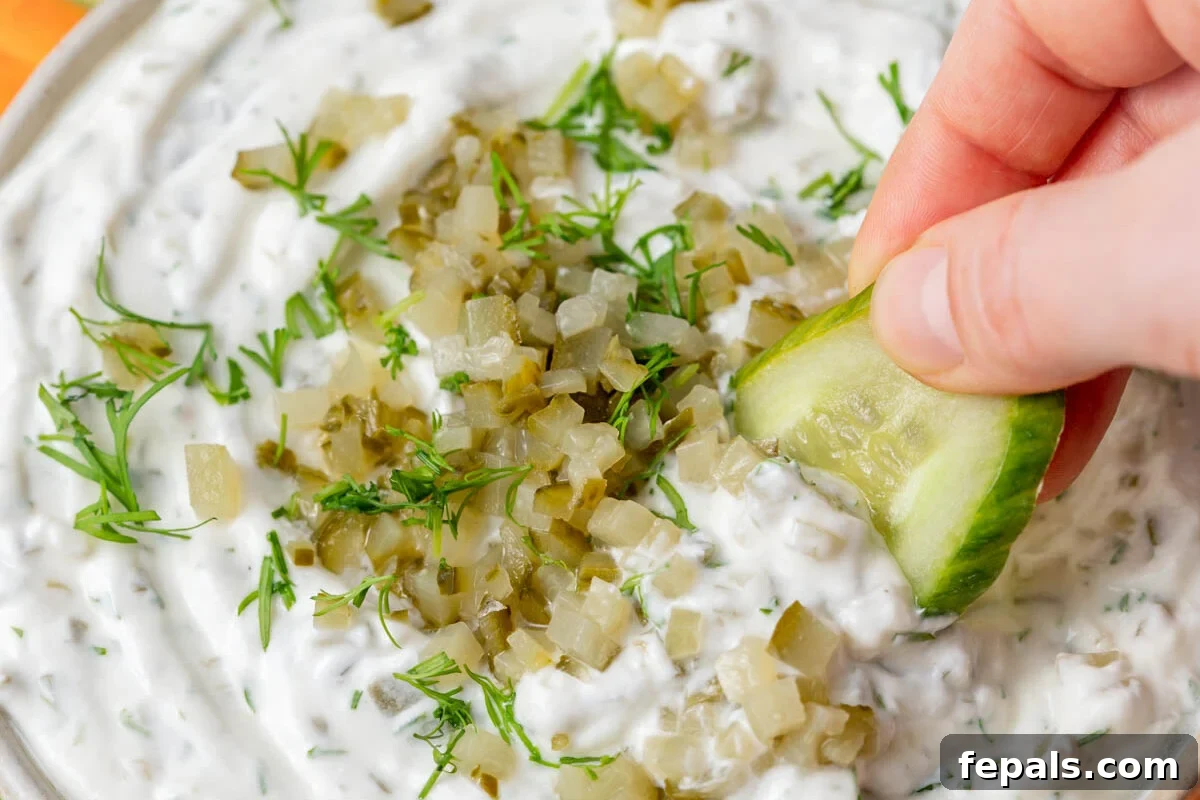 a hand dipping cucumber into the dill pickle yogurt dip.
