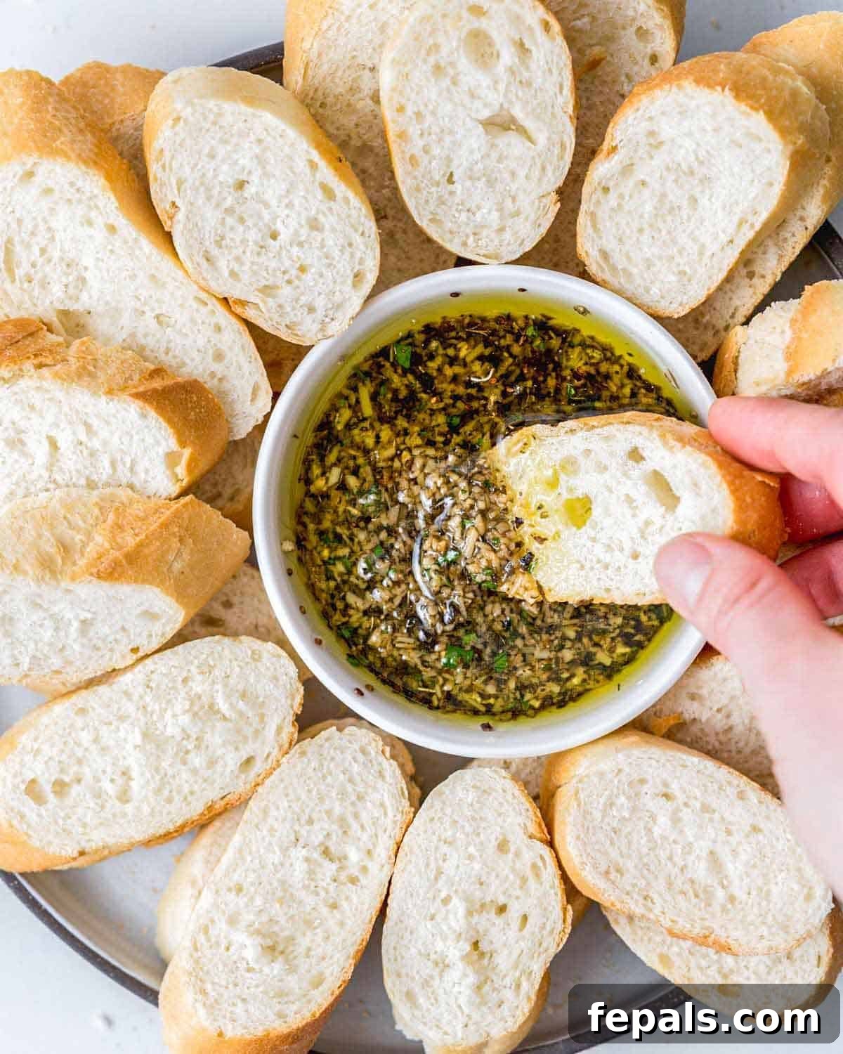 hand holding a piece of bread being dipped in olive oil bread dip.