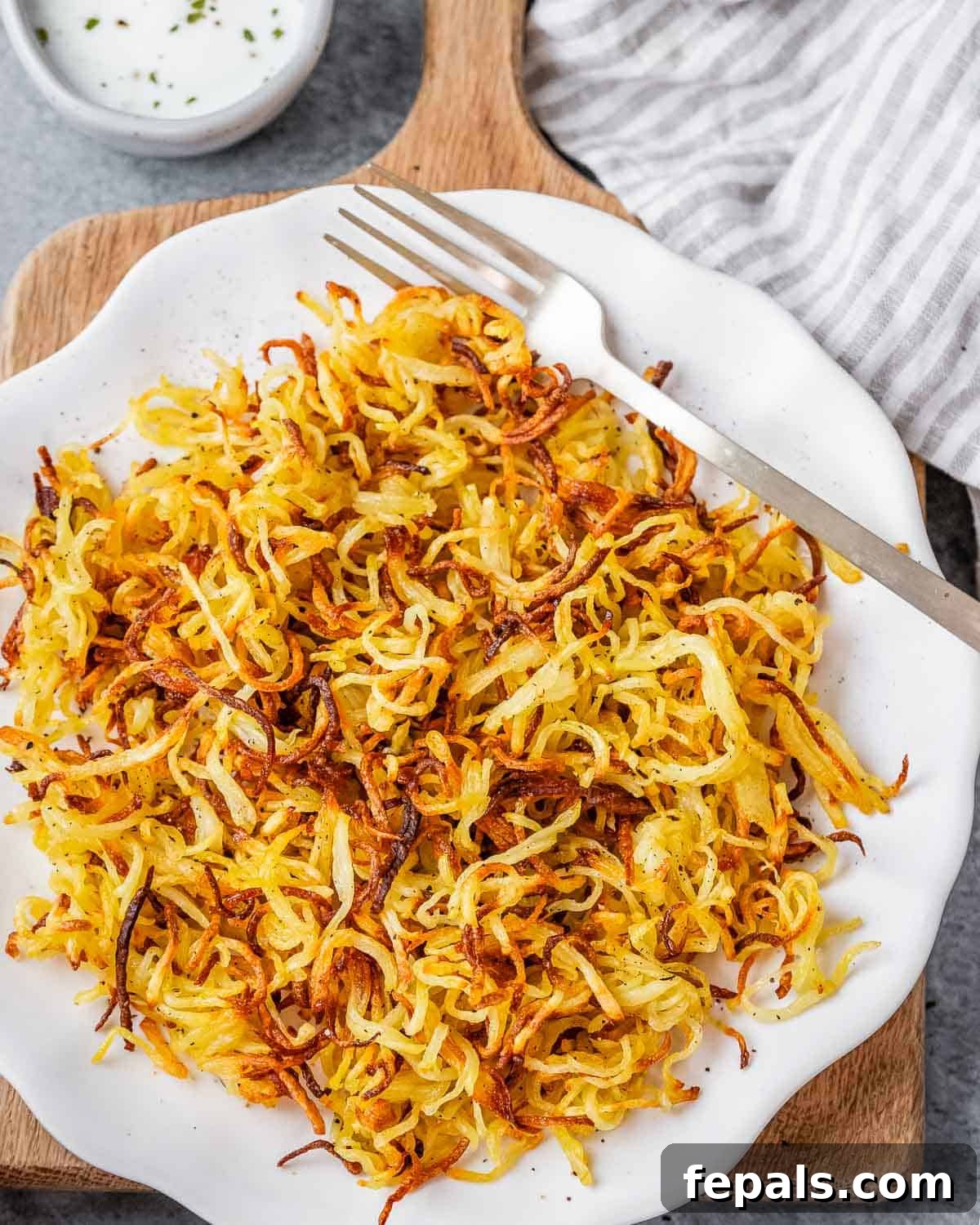 Crispy Air Fryer Frozen Hash Browns Recipe 2 Air fried hash browns on a white plate with a fork and striped napkin.