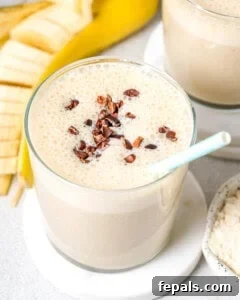 a glass filled with banana protein shake topped with cocoa nibs and a straw in the cup.