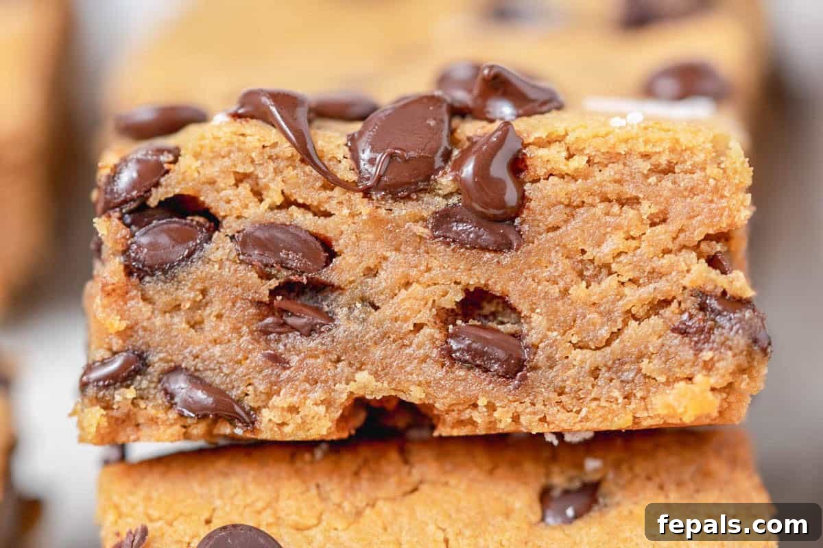 High-Protein Chocolate Chip Cookie Bars for Snackable Energy 6 a cookie bar laid over another cookie bar with visible melted chocolate chips on it.