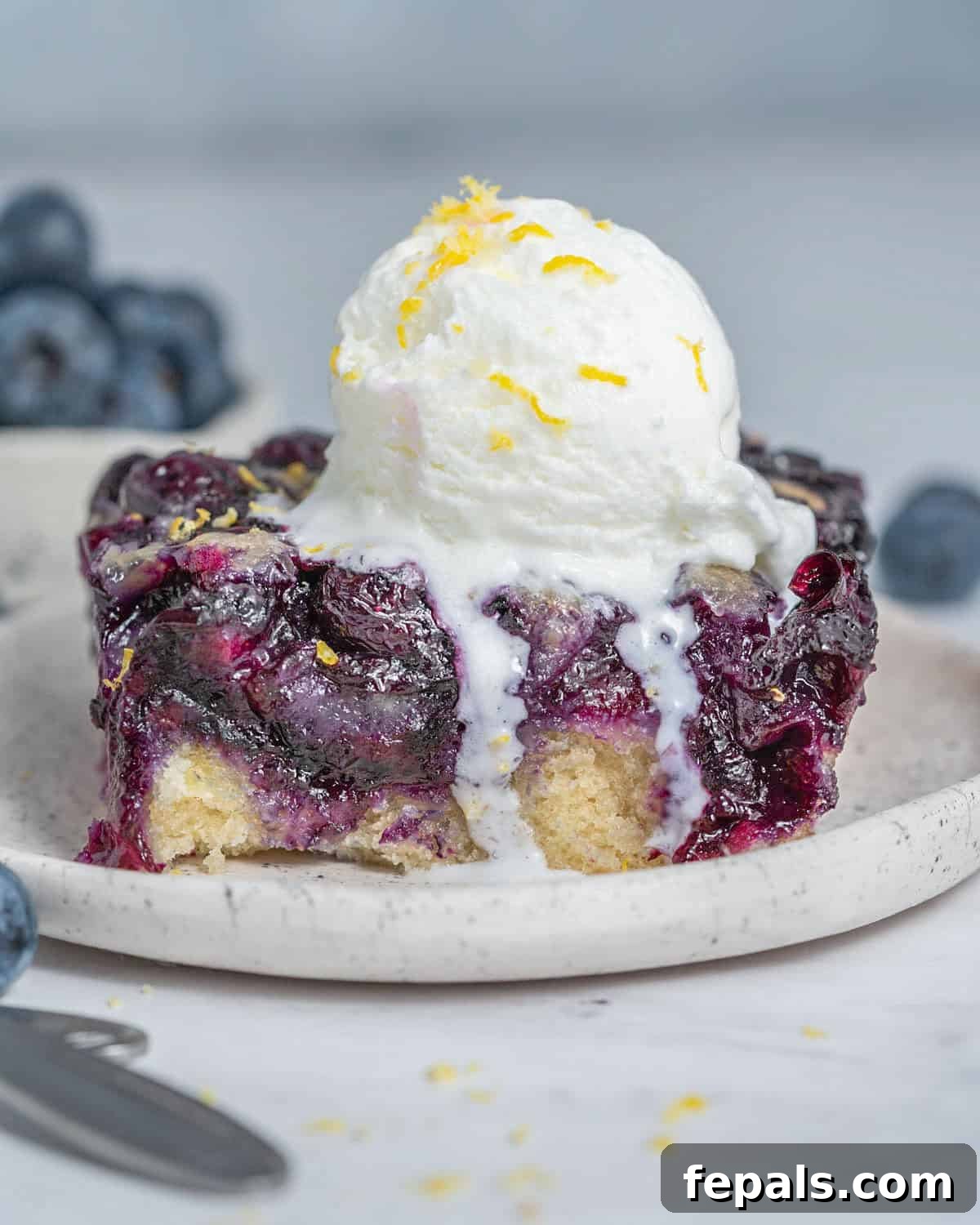 Classic Blueberry Cobbler Recipe 2 a slice of blueberry cobbler on a plate with a serving of icecream over it.