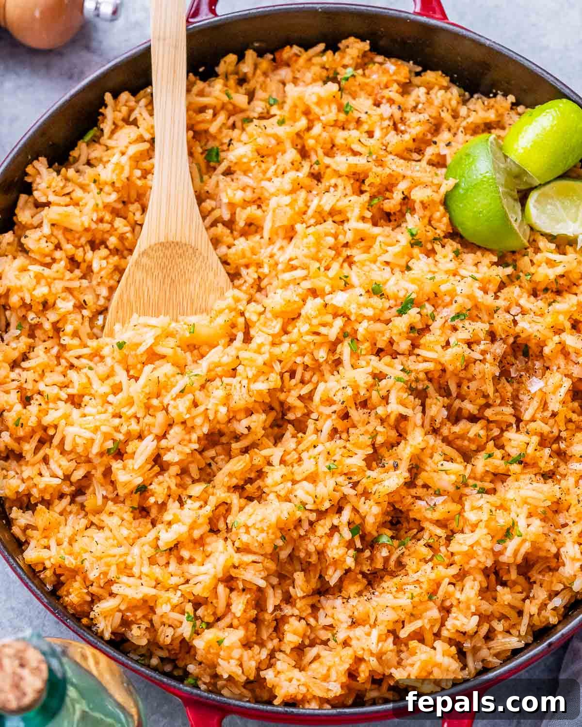 Mexican rice in a skillet with a wooden spoon and lime wedges.
