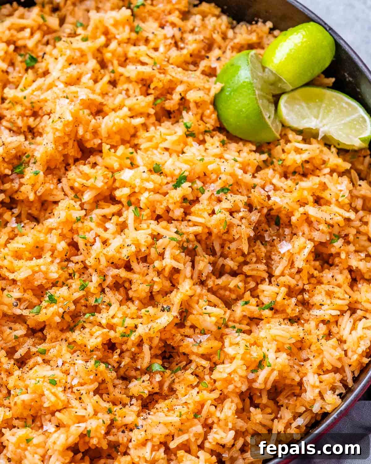 A skillet of Mexican rice with lime wedges.