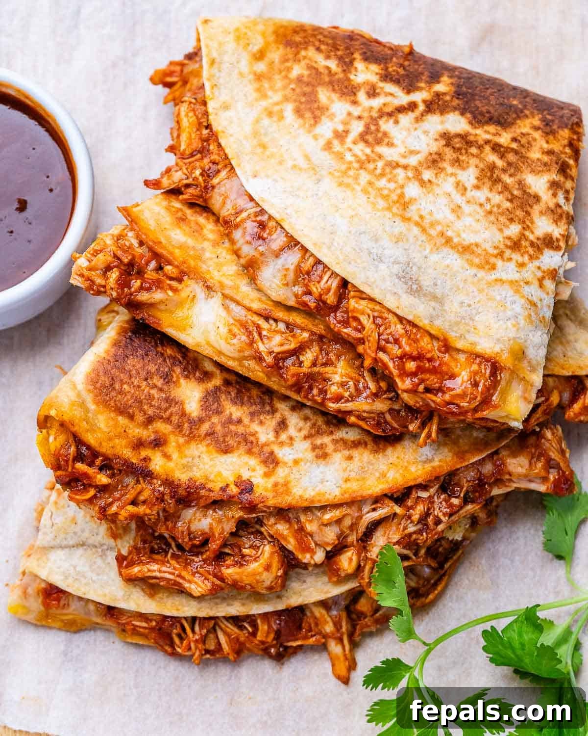 Copycat chipotle chicken quesadillas on parchment paper with a sprig of cilantro.