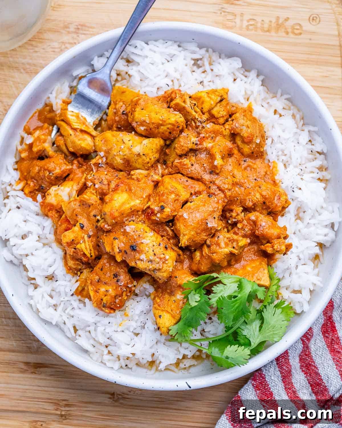 A white bowl of butter chicken over basmati rice.