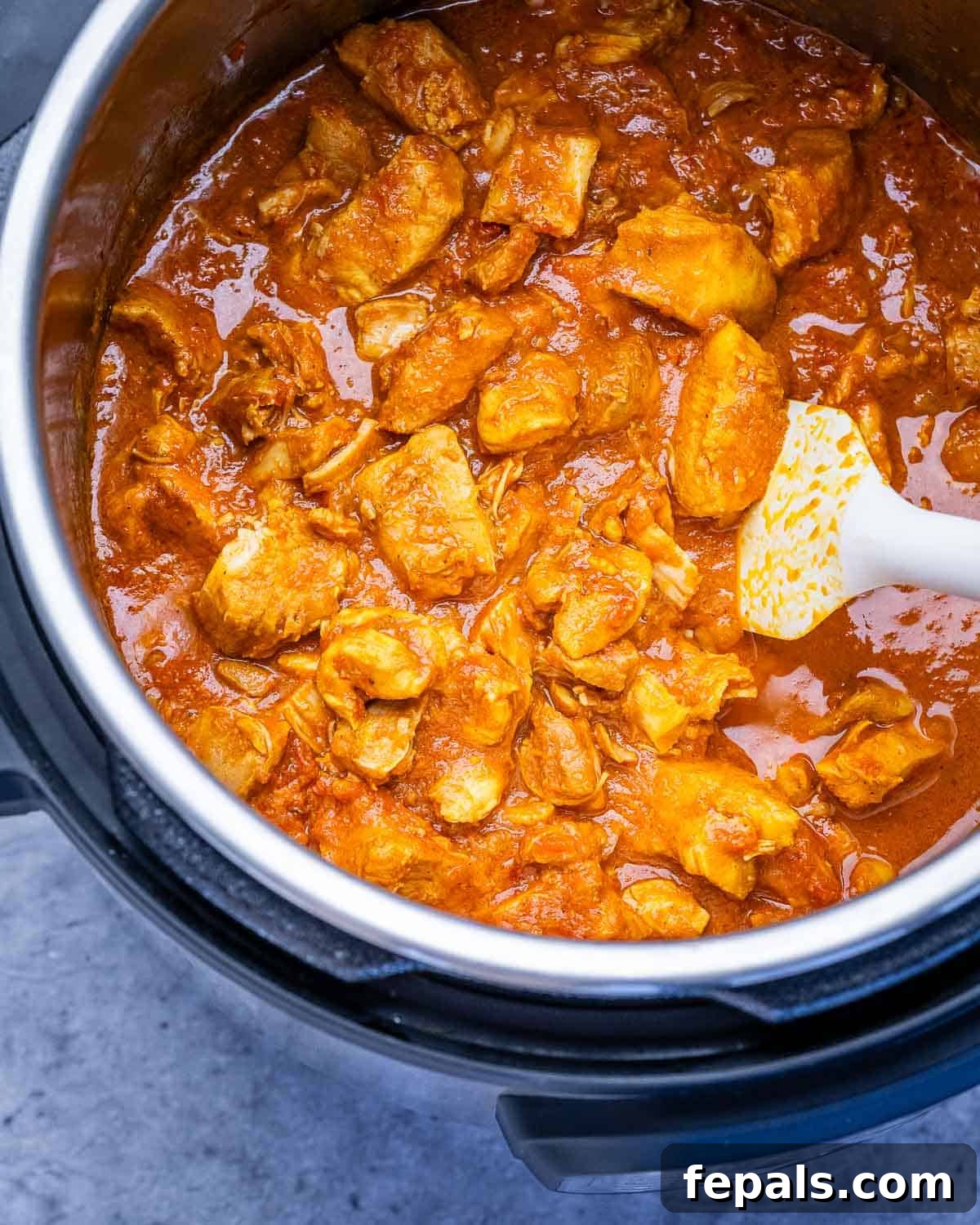 Butter chicken in an instant pot with a white spatula.