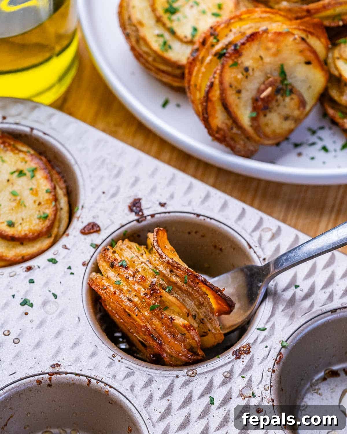 Crispy potato stacks in a muffin pan being scooped out with a spoon.