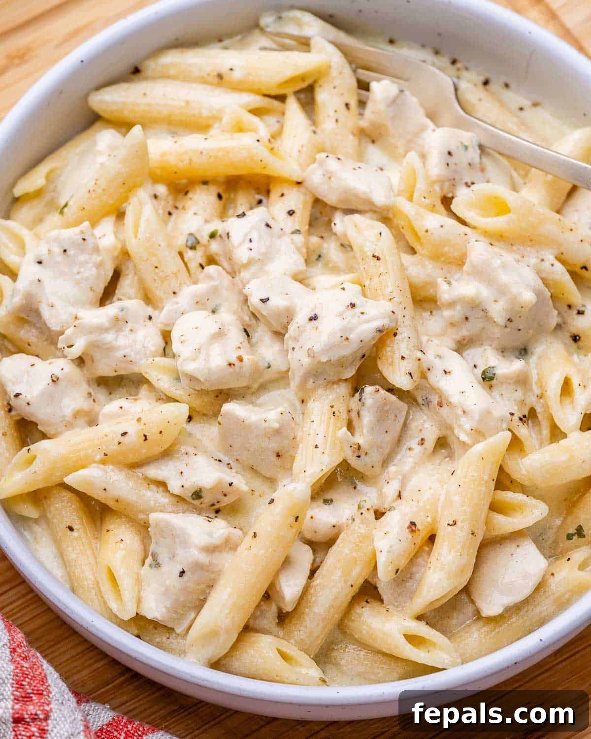 Slow cooker chicken alfredo with penne pasta in a white bowl.