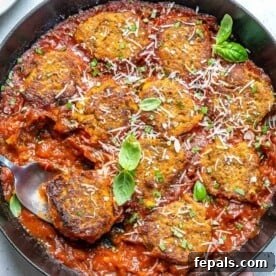 spoon in vegetarian meatballs in sauce in a black pan.