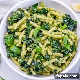 pesto pasta in a round white bowl with kale and basil leaf garnish.