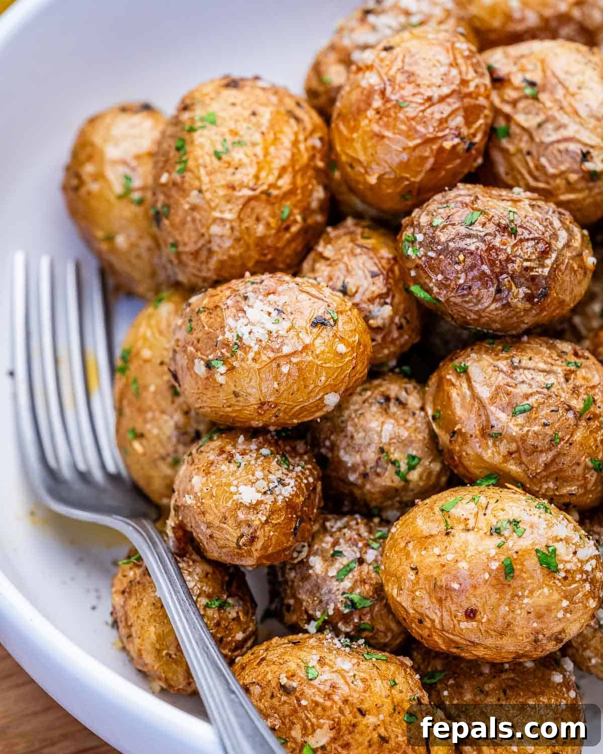 air fried potatoes added into a bowl with parmesan cheese and chopped parsley.