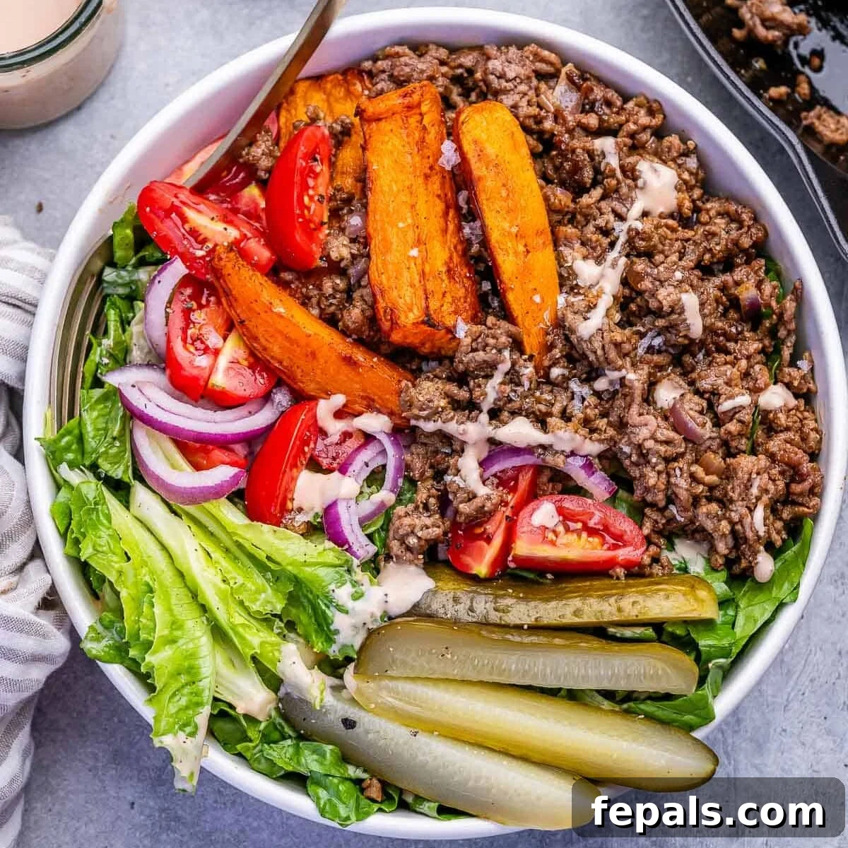 a bowl filled with lettuce, topped with seasoned beef and burger topping ingredients.