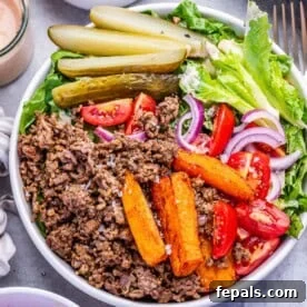 a bowl with cheeburger ground beef and lettuce topped with sweet potato fries, tomatoes, and sliced pickles.