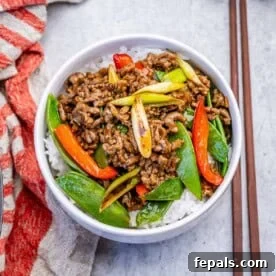 a bowl filled with rice topped with ground beef stir fry , snap peas, and red peppers.