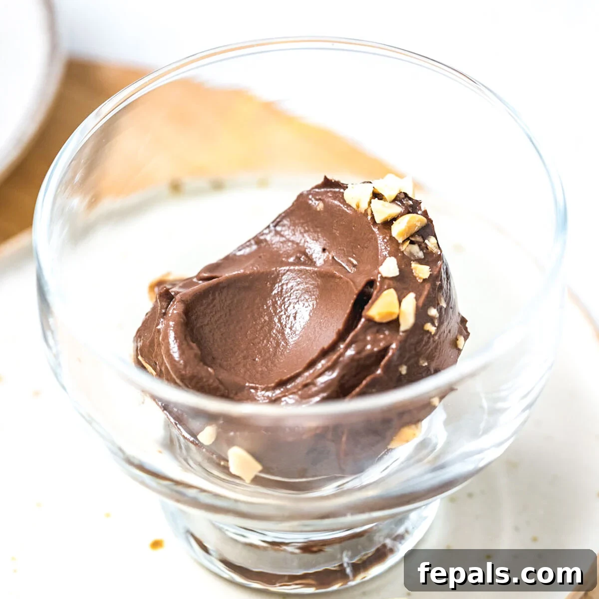 a glass bowl with avocado ice cream topped with chopped peanuts.