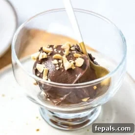 a clear bowl with avocado ice cream topped with chopped peanuts.