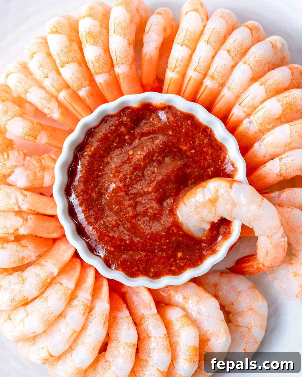 a bowl of homemade cocktail sauce surrounded by cooked cold shrimp.