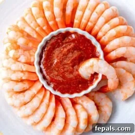 a bowl of cocktail sauce surrounded by cooked shrimp.