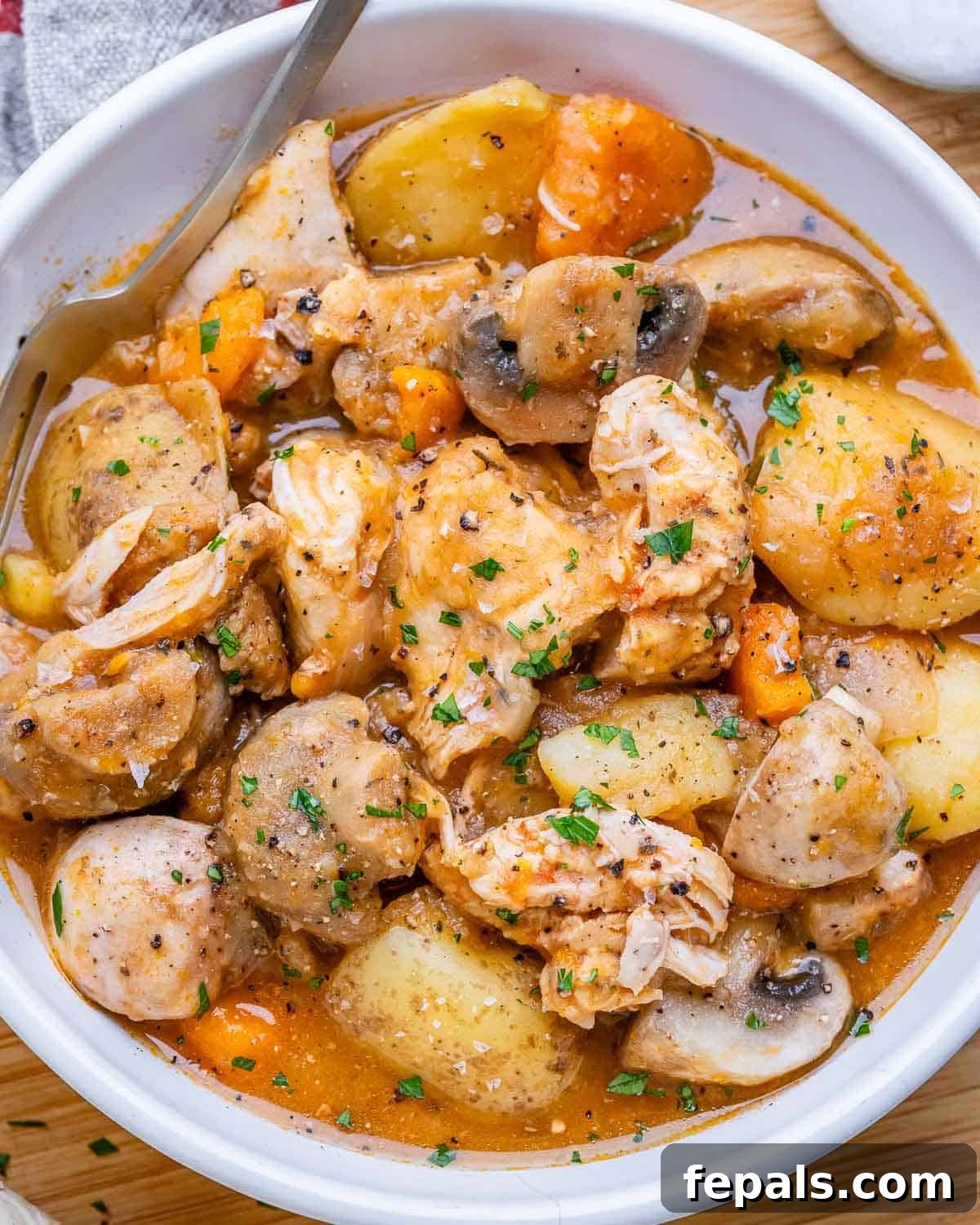 A white bowl of slow cooker chicken stew with potatoes and mushrooms.