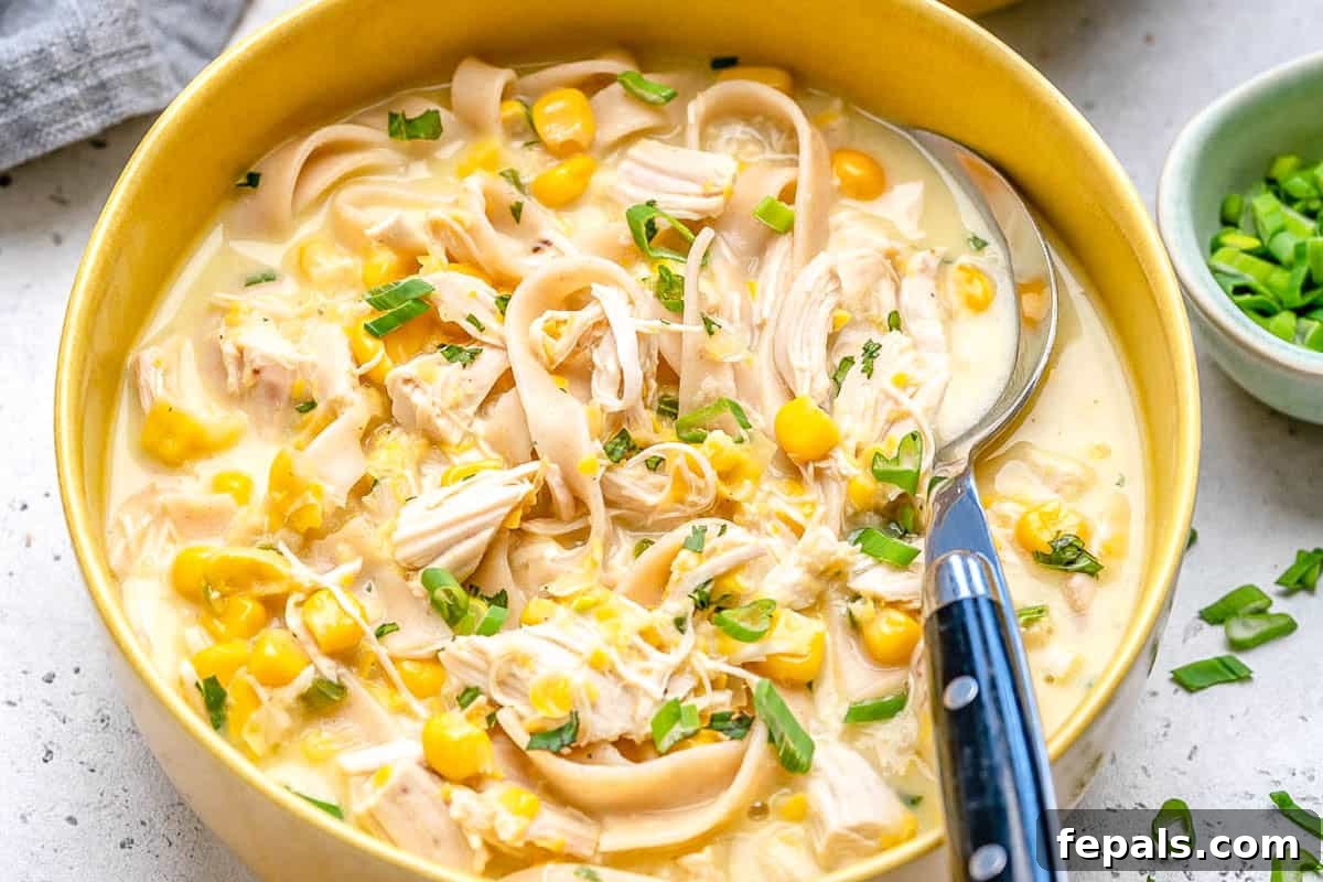 Creamy Rotisserie Chicken and Corn Soup 3 a yellow bowl with chicken corn soup and a spoon in the bowl.