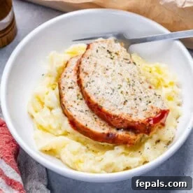 a serving of mashed potatoes topped with 2 slices of chicken meatloaf in a round bowl.