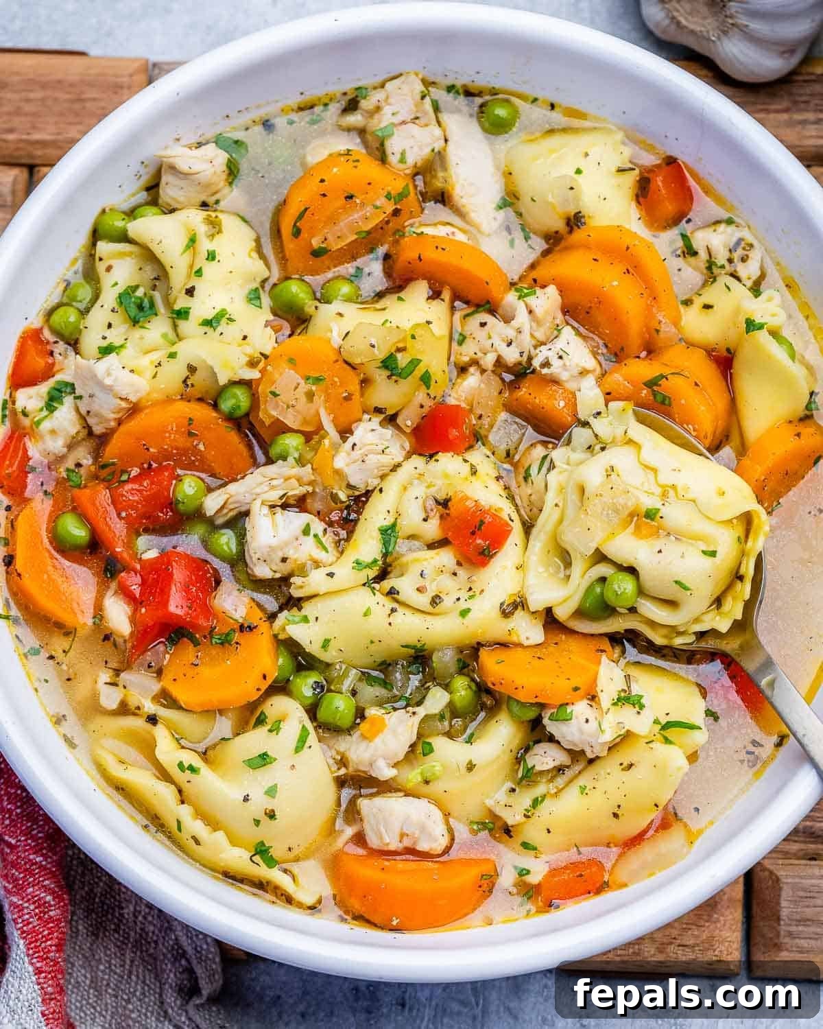 a bowl filled with chicken tortellini soup with carrots and peas.
