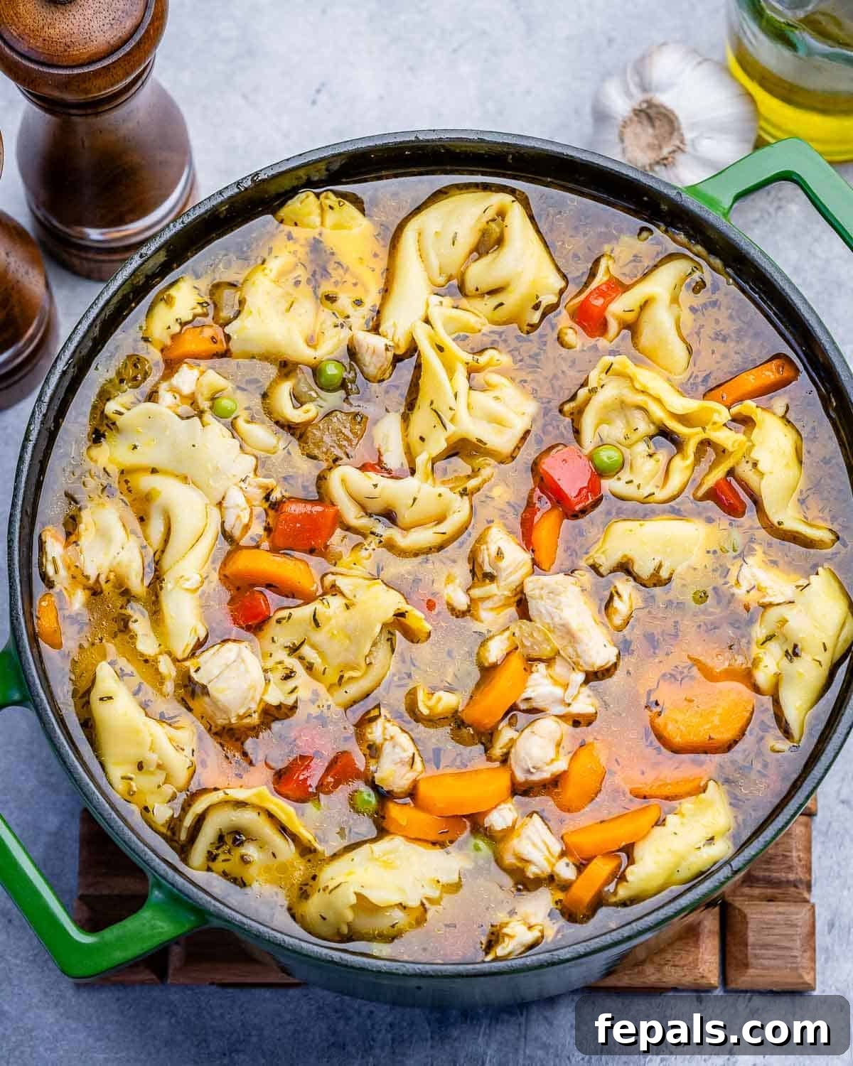 A green pot filled with chicken tortellini soup.