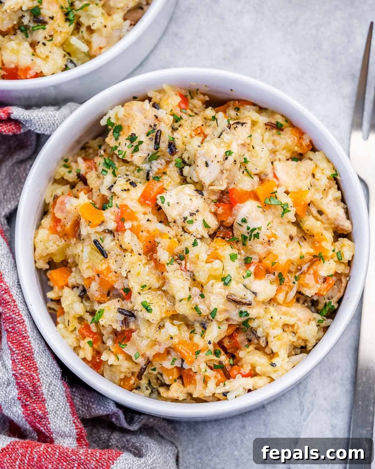 A white bowl of slow cooker chicken and rice next to a striped napkin.