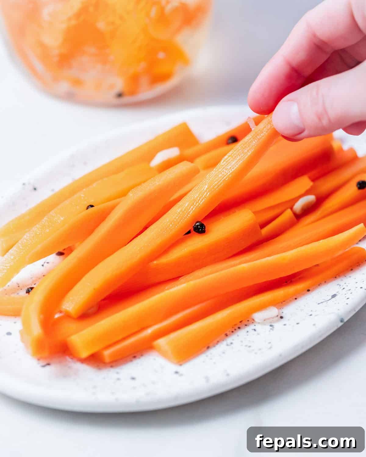 Crisp Homemade Pickled Carrots - Refrigerator Pickles Recipe 6 Hand grabbing a pickled carrot stick from a plate.