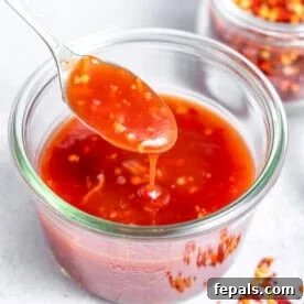 a jar with sweet chili sauce with a spoonful digging into the bowl.