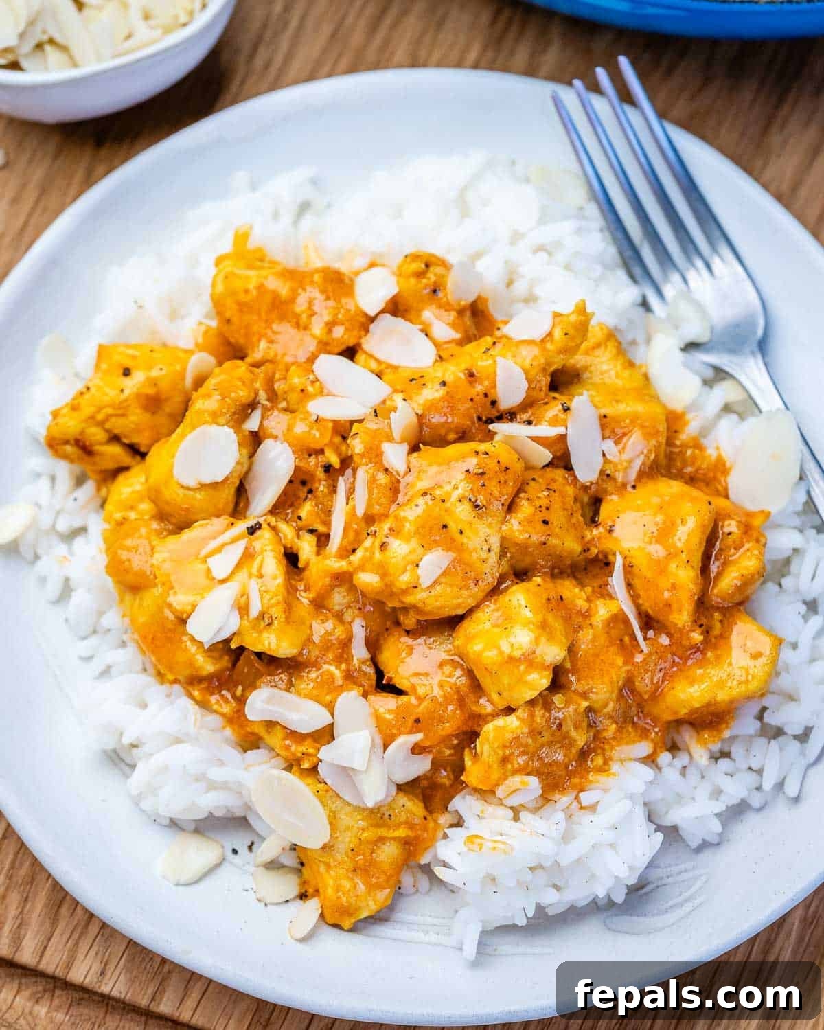 Creamy Chicken Korma with Greek Yogurt 7 A white bowl with rice and chicken korma topped with flaked almonds.