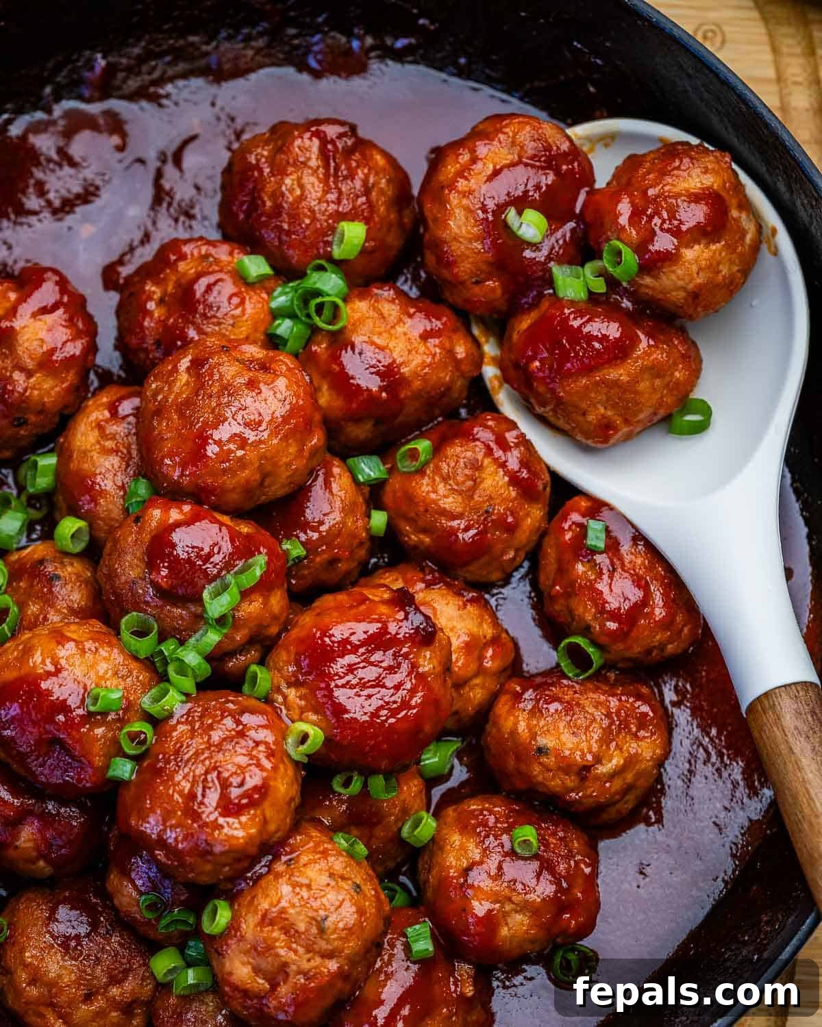 A skillet of grape jelly meatballs garnished with green onions.