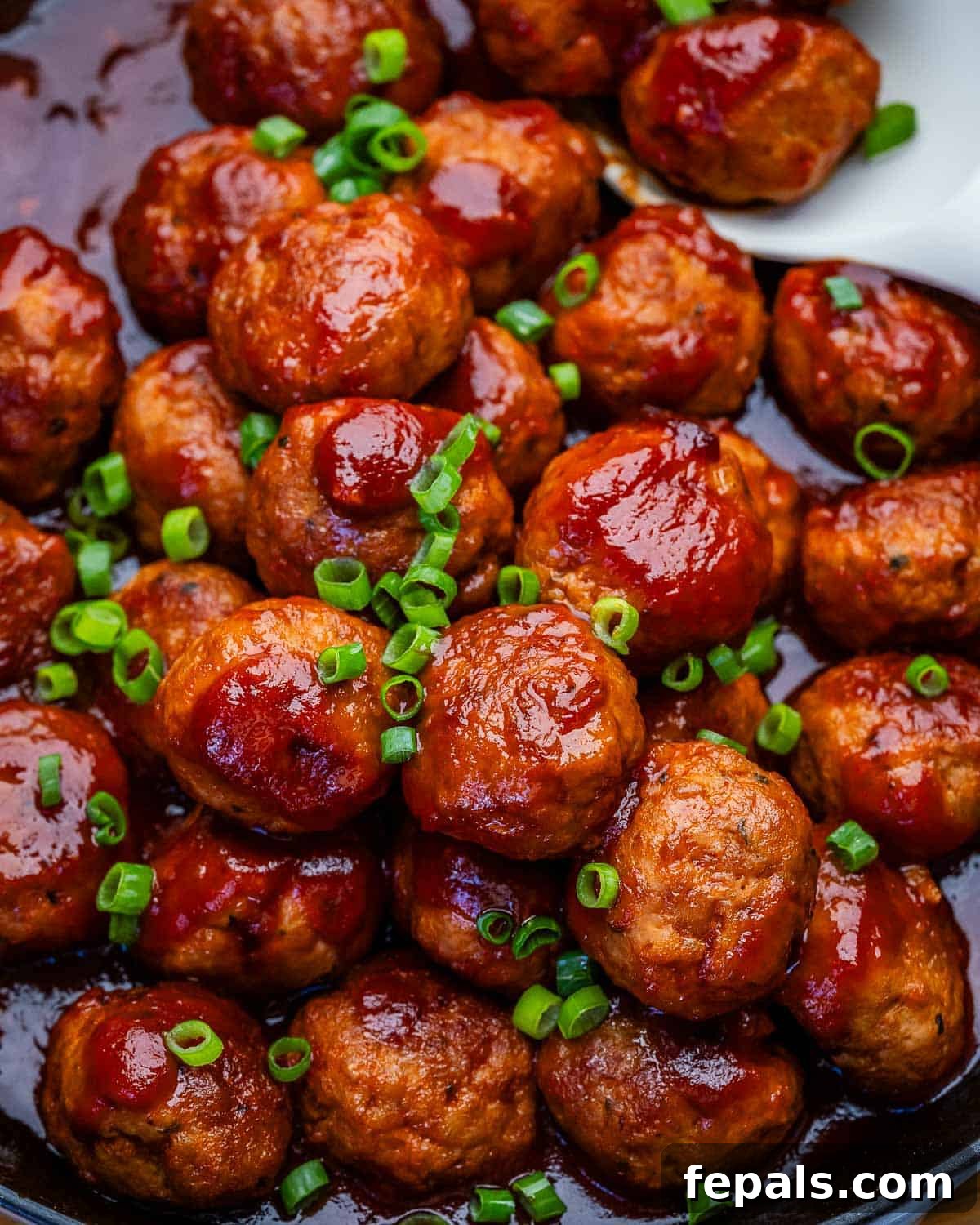 Grape jelly meatballs in a skillet with a white spoon.