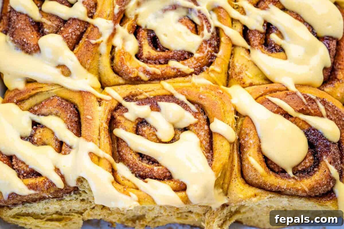 baked pumpkin cinnamon rolls in a dish with the yogurt pumpkin glaze.
