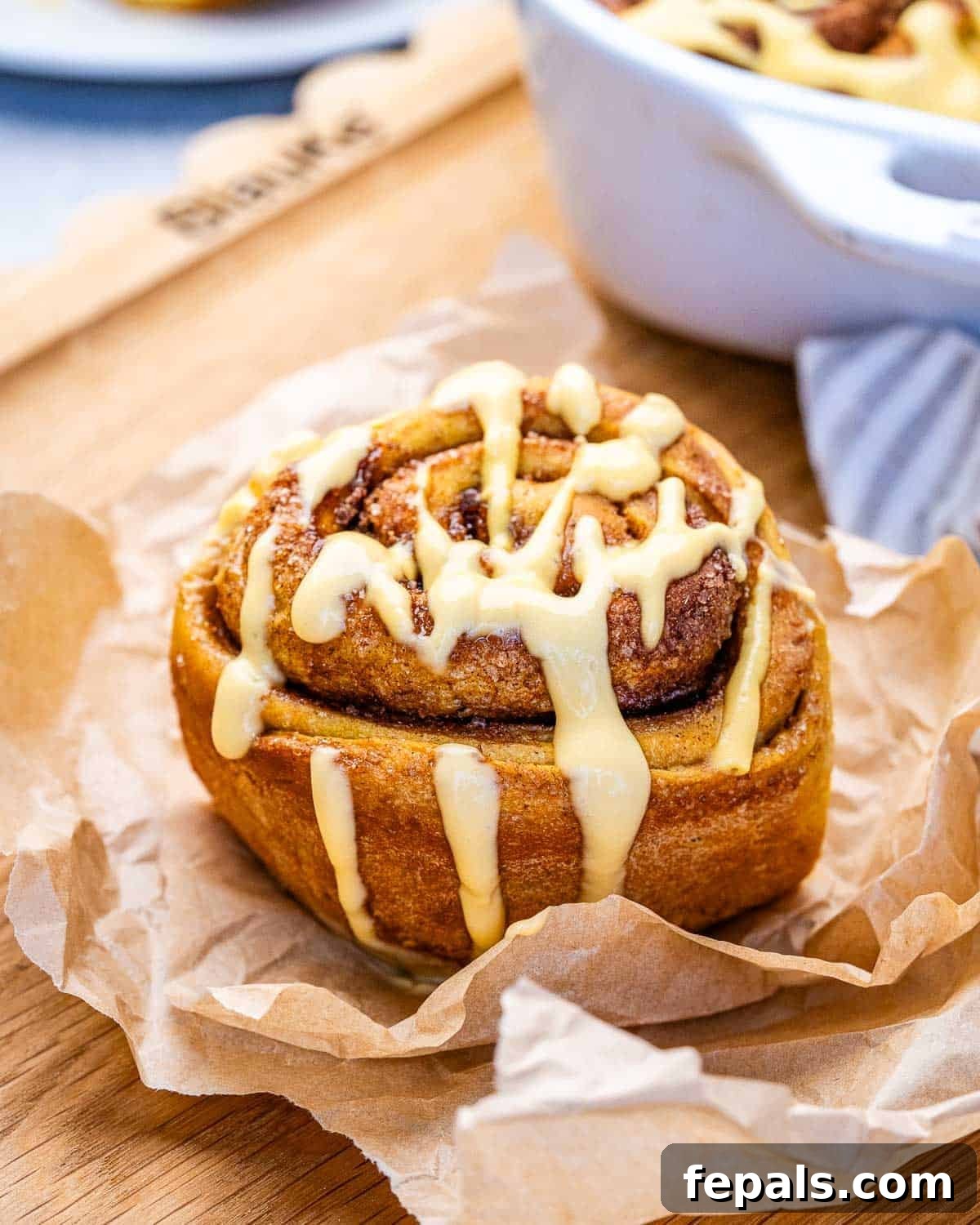 A pumpkin cinnamon roll drizzled with glaze, on a piece of parchment paper on a wooden board.