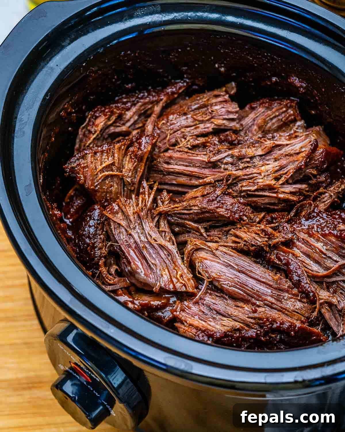 A slow cooker filled with shredded beef chuck roast.