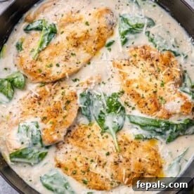 top view of creamy chicken breast with spinach in a black skillet