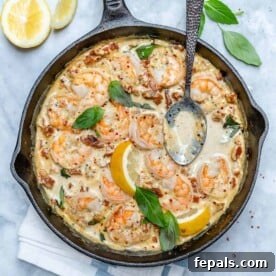top view of Tuscan shrimp in a creamy sauce in black skillet with metal spoon in skillet and on top left there are 2 lemon wedges next to the skillet
