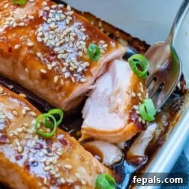 side shot of a fork getting a morsel of the baked teriyaki salmon from a white baking dish